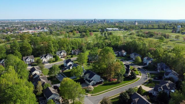 An aerial view of a suburban neighborhood with tree-lined streets and a skyline in the background.