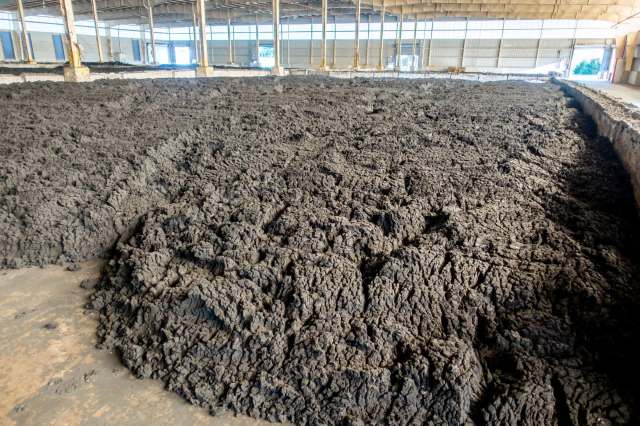 A large area of dark, uneven, dried sludge in a spacious indoor facility.