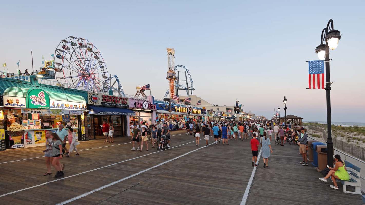 A busy boardwalk lined with shops and a Ferris wheel.