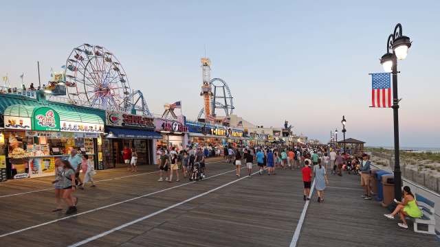 A busy boardwalk lined with shops and a Ferris wheel.
