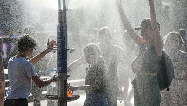 People enjoying a water mist fountain on a sunny day, with spray creating a refreshing atmosphere.