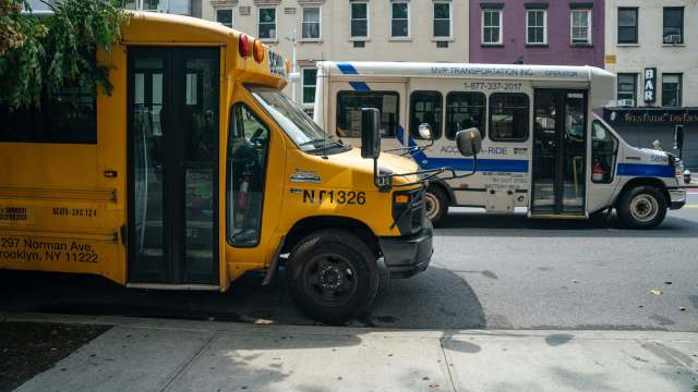 A yellow school bus and a blue and white transport bus parked side by side on a city street.