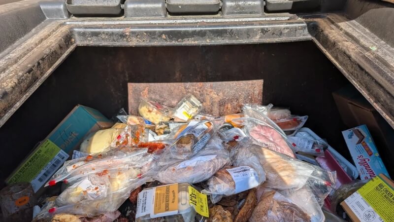 A pile of packaged food in an open dumpster.