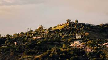 A hillside dotted with houses and lush greenery under a partly cloudy sky.