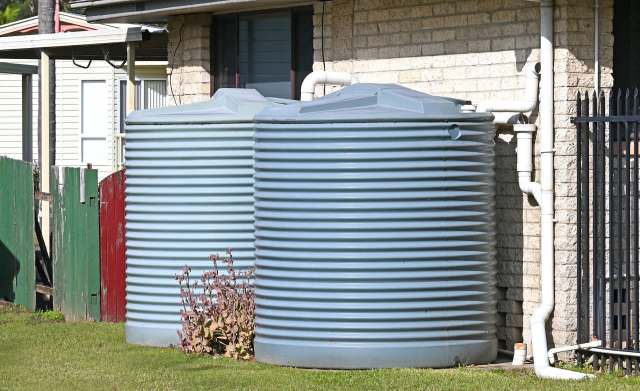 Two large rainwater tanks sit beside a house with a grass lawn.