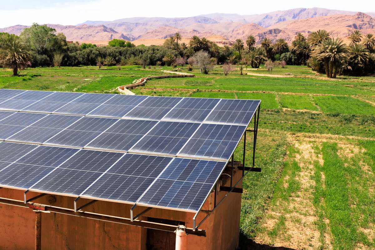 A rooftop covered with solar panels overlooks lush green fields and distant mountains.