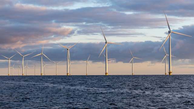 A row of wind turbines stands in the ocean under a cloudy sky at sunset.