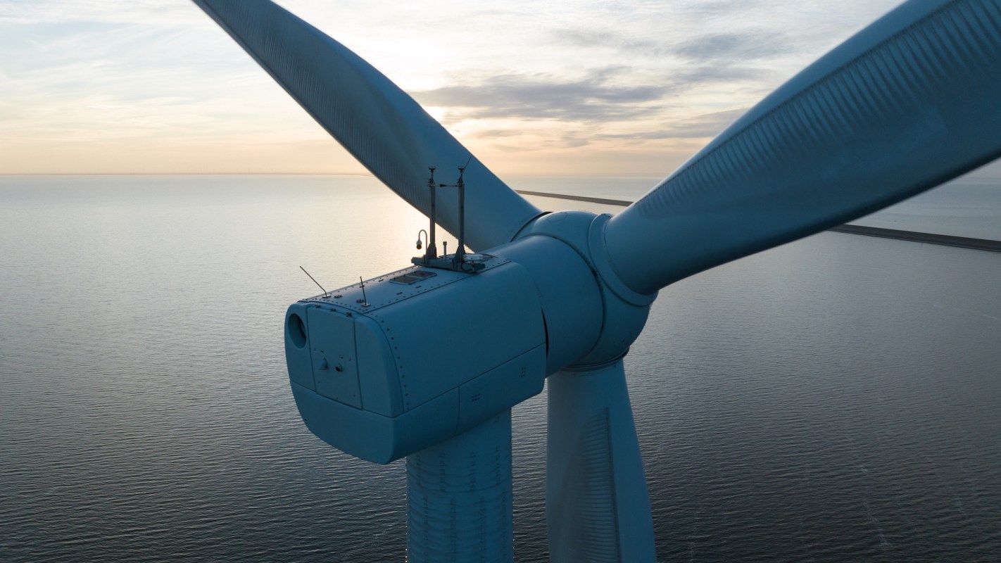 A close-up view of a wind turbine against a serene ocean backdrop during sunset.