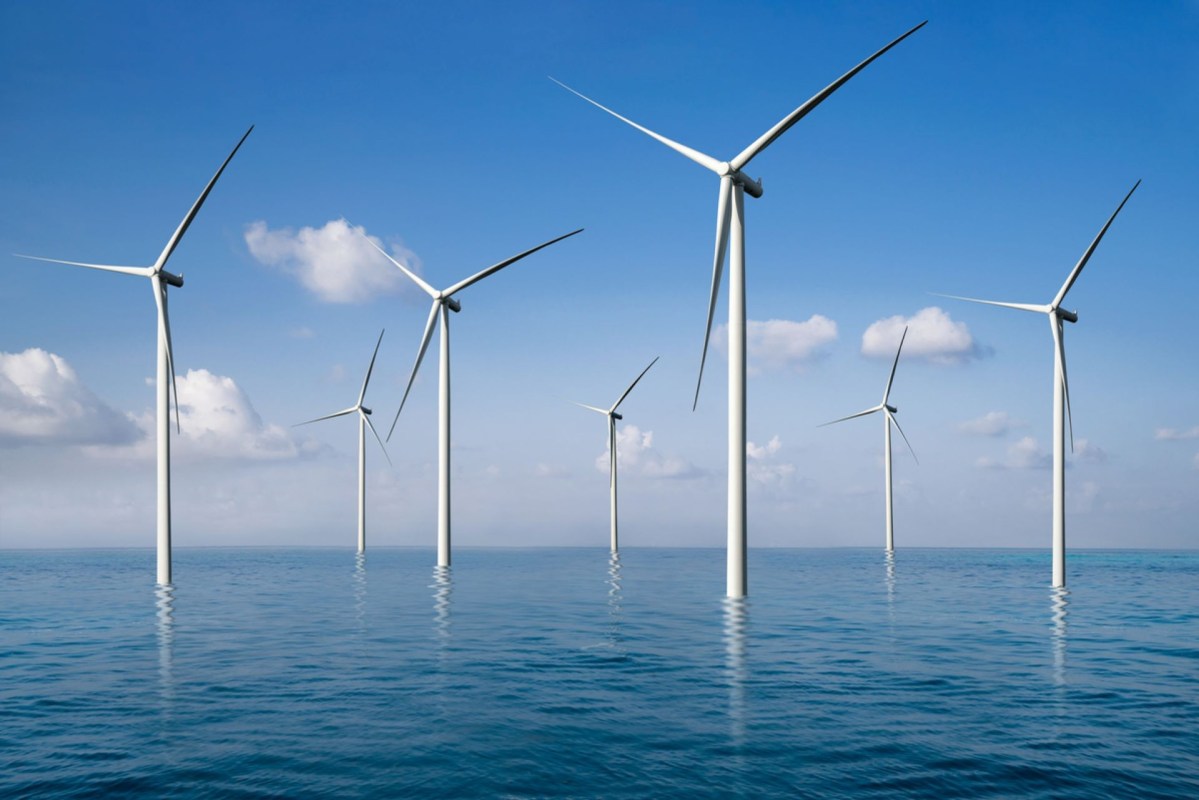 A row of wind turbines stands in a calm ocean under a clear blue sky with a few clouds.