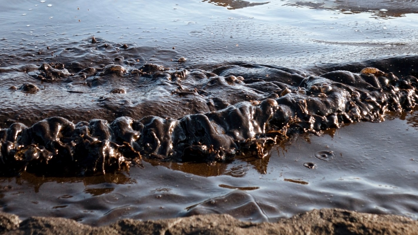 A close-up view of dark, glossy oil washing over a rocky shore.