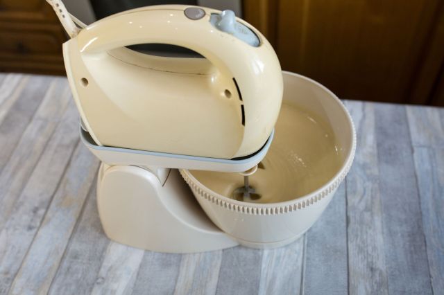 An electric hand mixer rests on a countertop with a mixing bowl beneath.