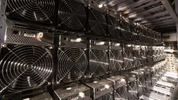 A row of crypto mining machines lined up in a data center, featuring cooling fans and network connections.
