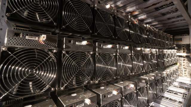 A row of crypto mining machines lined up in a data center, featuring cooling fans and network connections.