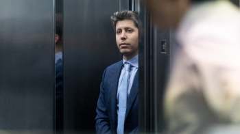 A man in a business suit stands quietly in an elevator, reflecting a serious expression.