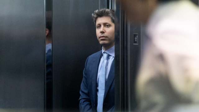 A man in a business suit stands quietly in an elevator, reflecting a serious expression.