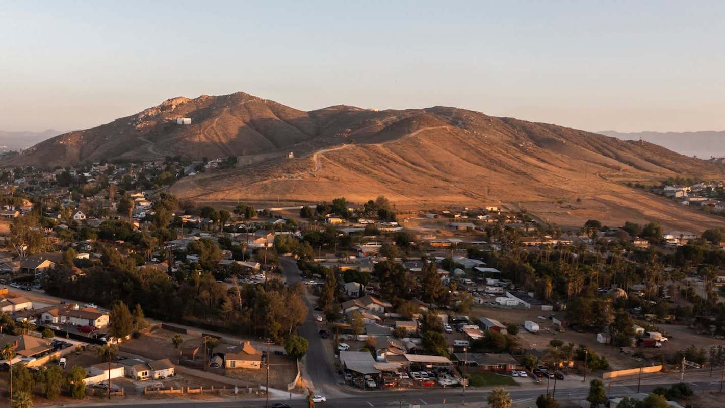 Aerial view of a mountainous landscape with residential areas and sparse vegetation at sunset.