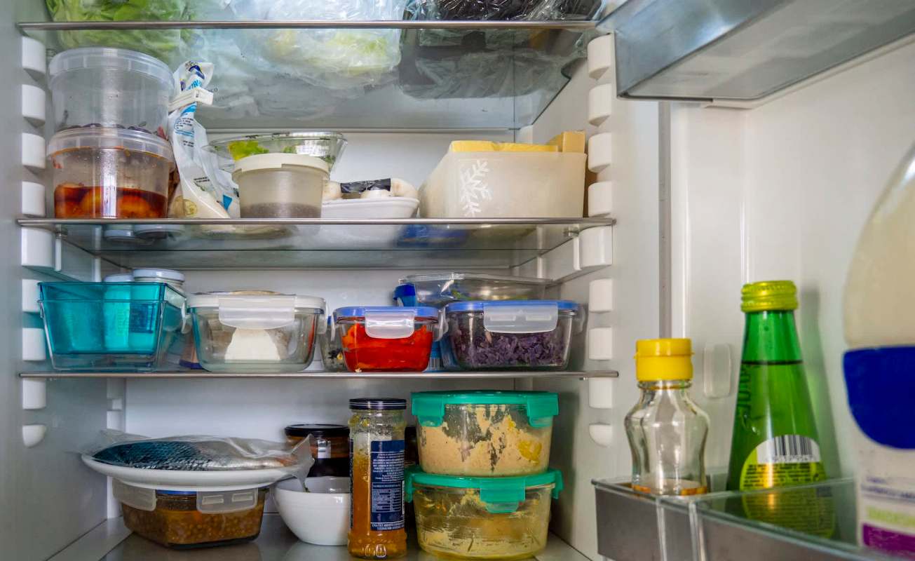 A refrigerator filled with various food containers, bottles, and fresh produce on different shelves.