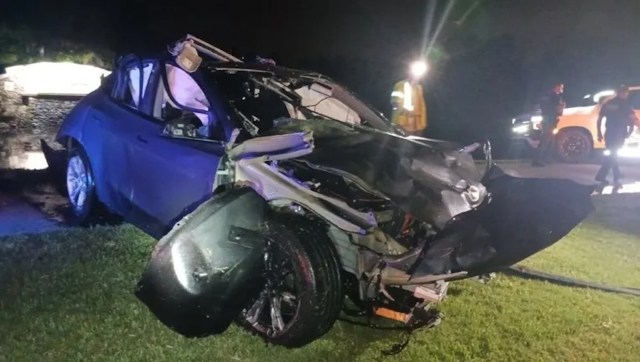 A severely damaged car on its side at night, with first responders visible in the background.