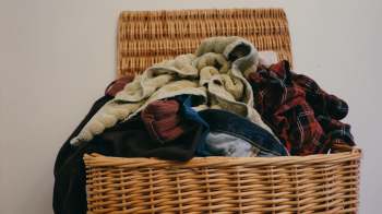 A overflowing wicker laundry basket filled with assorted clothes and towels.