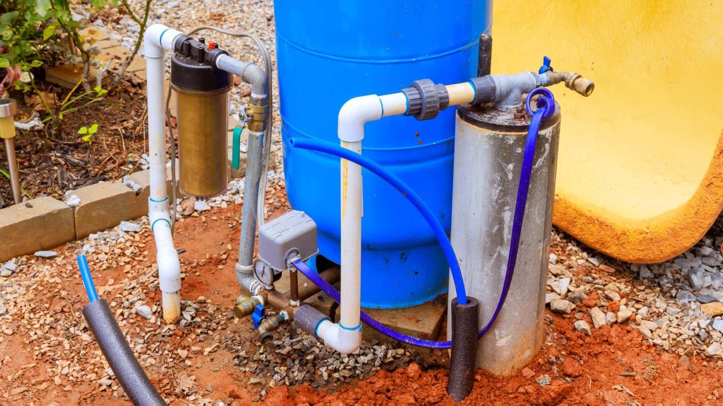 A blue well water tank system connected to pipes and a filter over gravel.