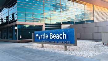 A sign for Myrtle Beach International Airport in front of a modern glass building.