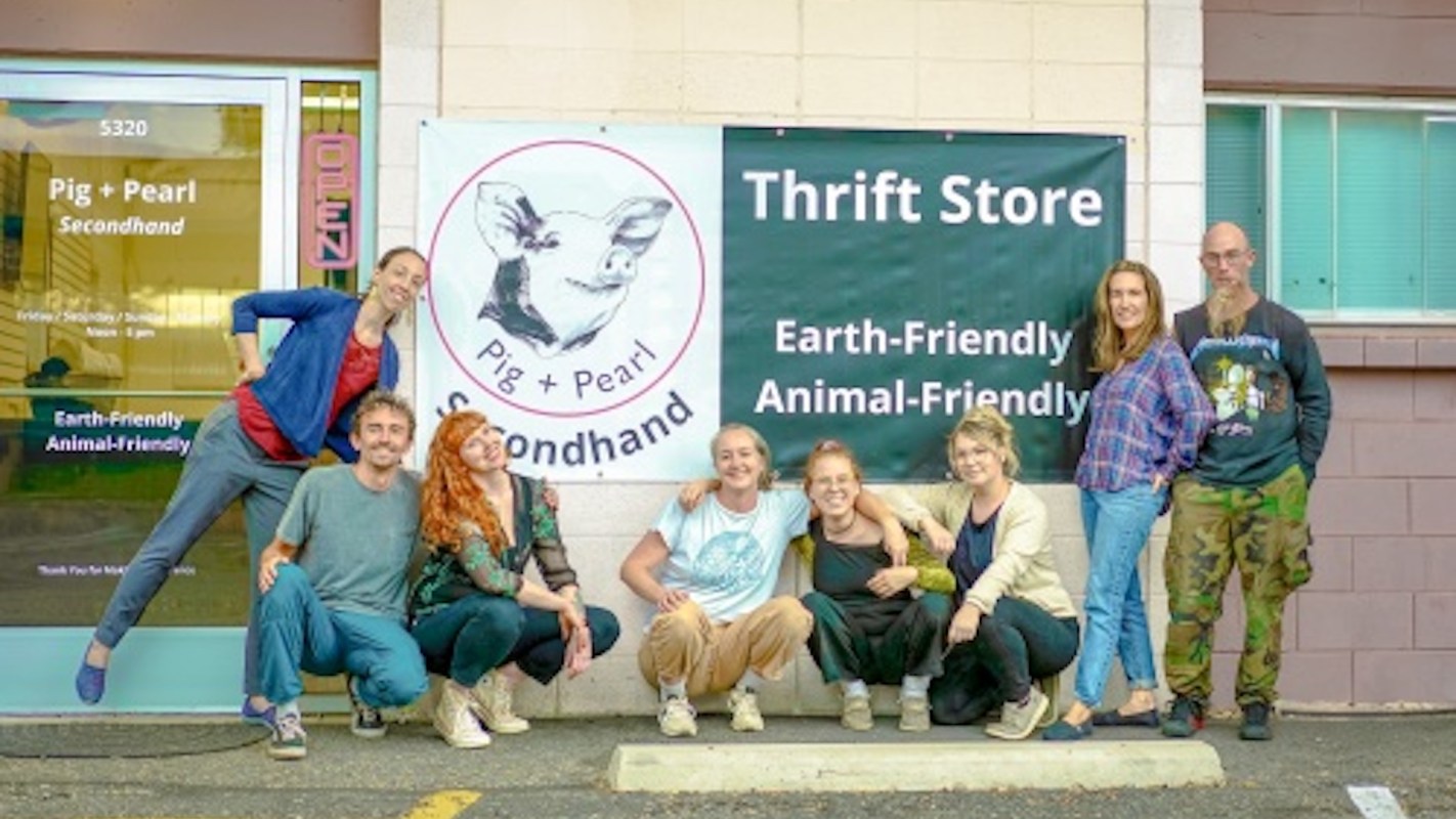 A group of eight individuals poses in front of the Pig + Pearl thrift store, showcasing a welcoming atmosphere.