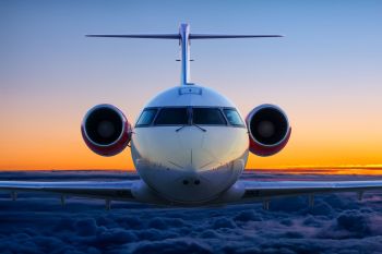 A front view of an airplane flying above clouds during a vibrant sunset.
