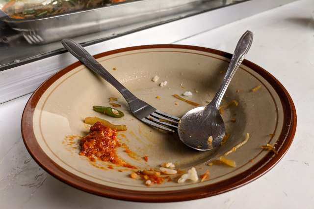 An empty plate with remnants of food, a fork, and a spoon.