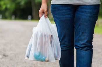 A person walking on a path holds a white plastic bag containing various items.