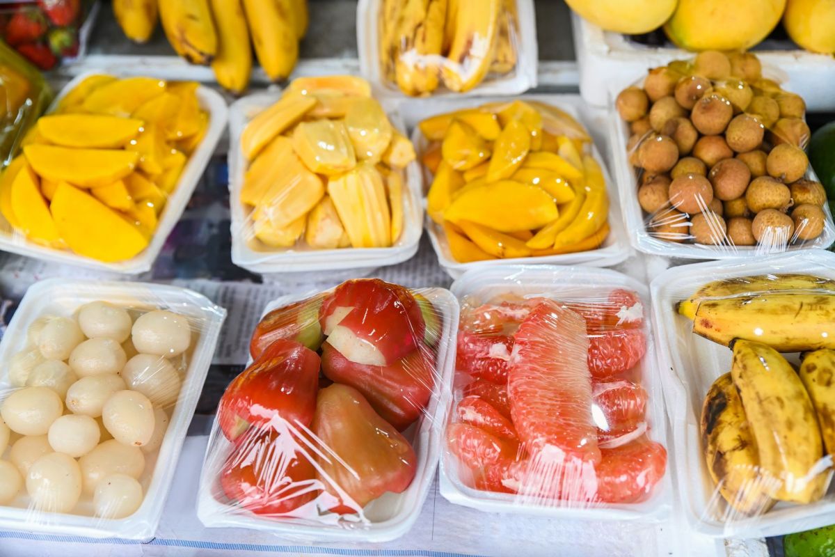 A variety of tropical fruits in plastic containers, including mangoes, bananas, and guavas, displayed in a market.