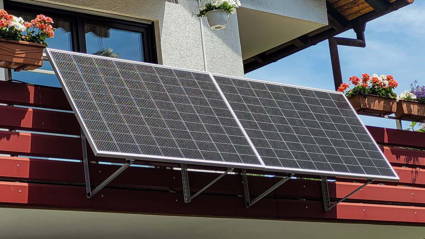 Two solar panels mounted on a balcony railing next to flower pots.