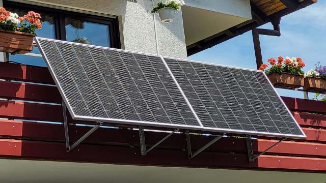 Two solar panels mounted on a balcony railing next to flower pots.