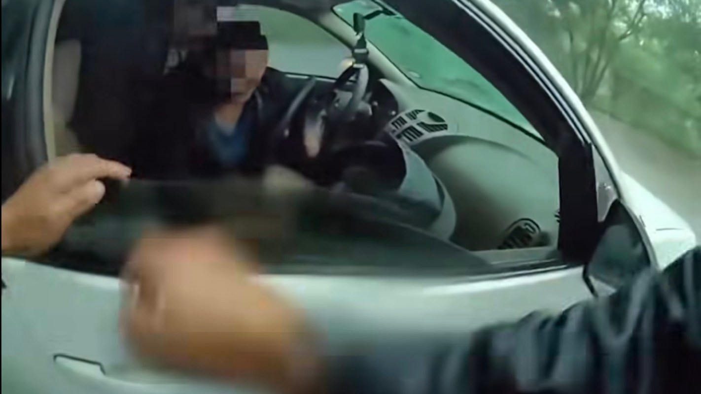 A driver leans toward a person approaching their vehicle's passenger window.