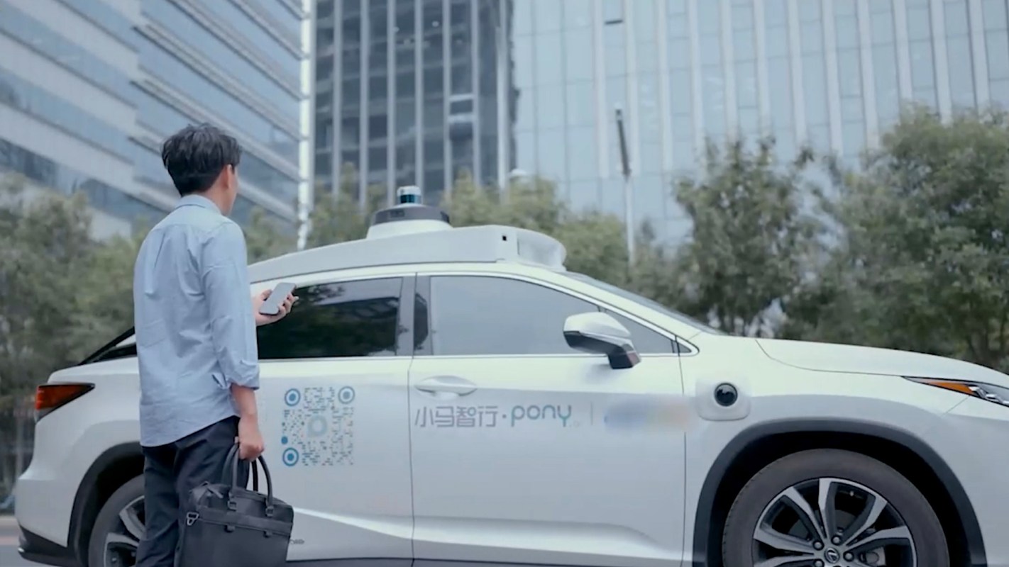 A man with a smartphone stands next to an autonomous vehicle.