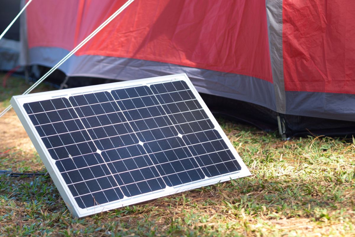 A solar panel leaning against a tent on grassy terrain.