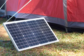 A solar panel leaning against a tent on grassy terrain.