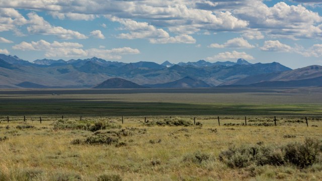 A vast landscape featuring rolling hills, grassy plains, and distant mountains under a partly cloudy sky.