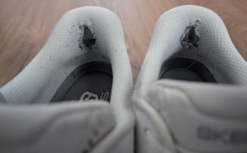A close-up of worn-out white sneakers showing torn fabric at the heel area.