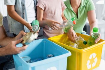 A family sorts recyclable materials into blue and yellow bins in a bright room.
