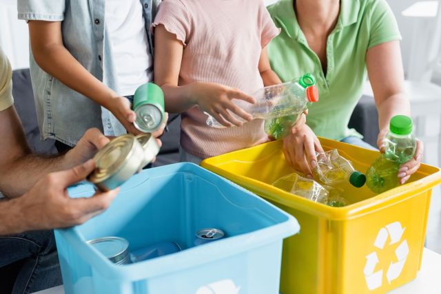 A family sorts recyclable materials into blue and yellow bins in a bright room.