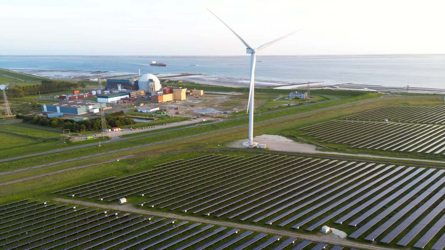 Solar panels with a wind turbine and a nuclear power plant near a coast.