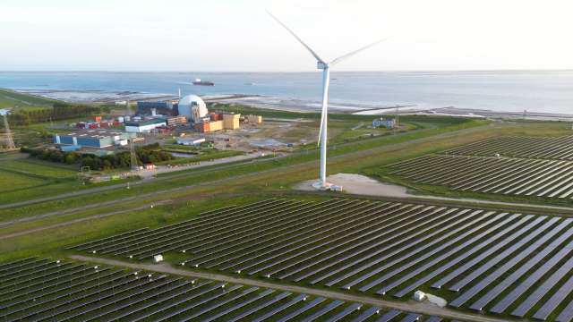 Solar panels with a wind turbine and a nuclear power plant near a coast.
