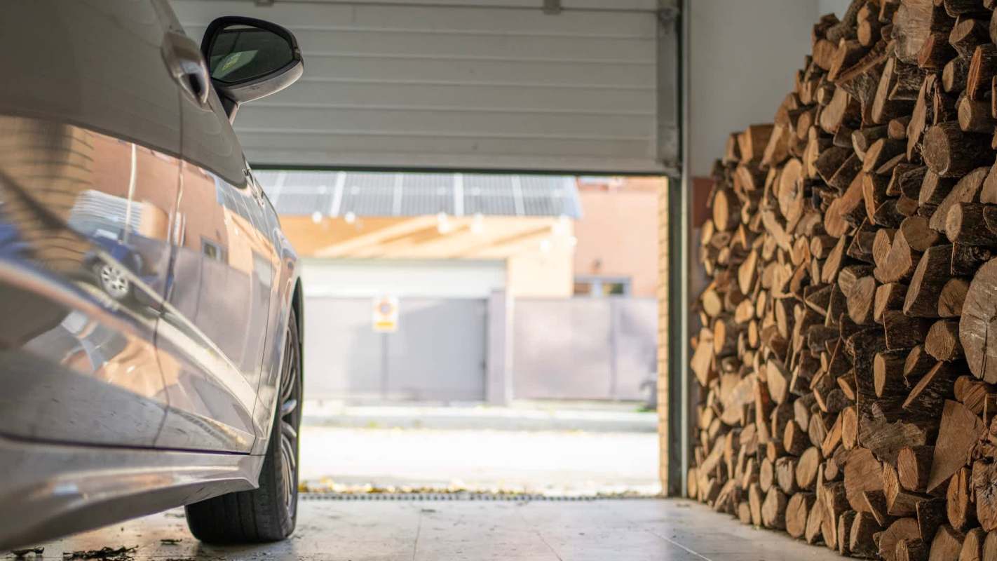 A car parked next to a pile of firewood in a partially opened garage.