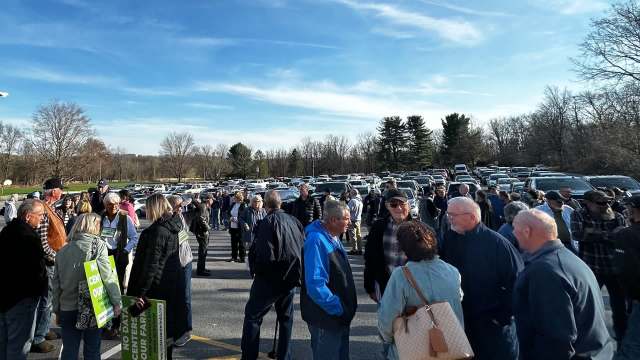 A crowd of people with signs gathered in a parking lot under a clear blue sky.