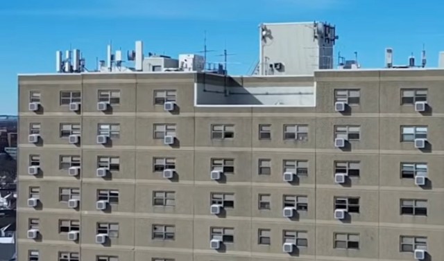 A close-up view of a tall building's wall featuring multiple air conditioning units and a clear blue sky above.