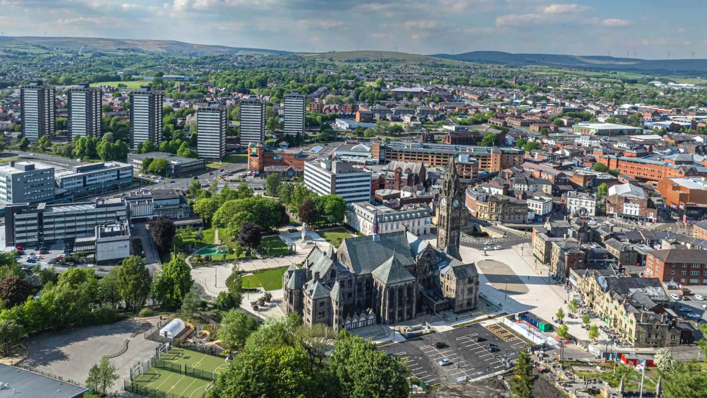An aerial view of a city featuring modern buildings, green spaces, and a historic church.
