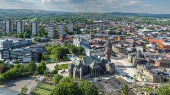 An aerial view of a city featuring modern buildings, green spaces, and a historic church.
