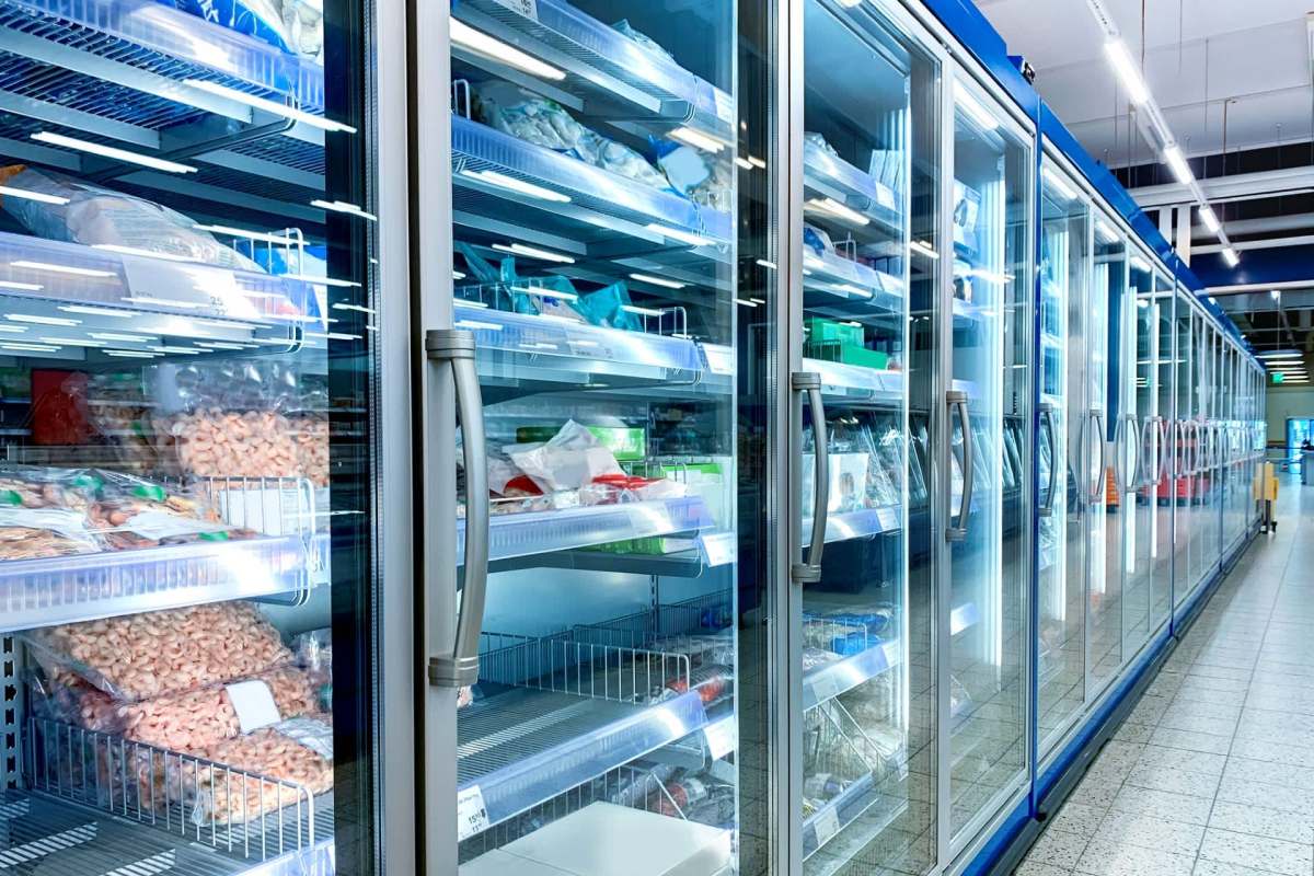 A row of glass-fronted freezer displays filled with assorted packaged frozen foods in a grocery store.