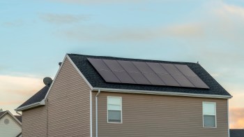A house with solar panels on the roof and a clear sky in the background.