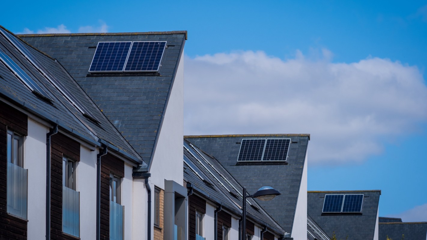Residential buildings with sloped roofs equipped with solar panels under a clear blue sky.